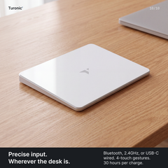 White rectangular glass touchpad with a Turonic logo sitting flat on a wooden desk beside a laptop corner.