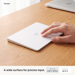 Two fingers gliding across a white rectangular glass touchpad resting flat on a wood desk.