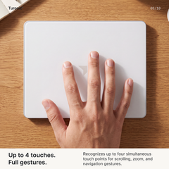 Four fingers and a thumb spread flat across the white glass surface of the touchpad on a wood desk.
