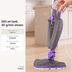 A hand pouring water into the purple and grey steam mop's tank opening, with the unit standing upright on a light wood floor.