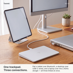White touchpad on a wood desk connected via USB-C cable to a tablet, monitor, and laptop simultaneously.